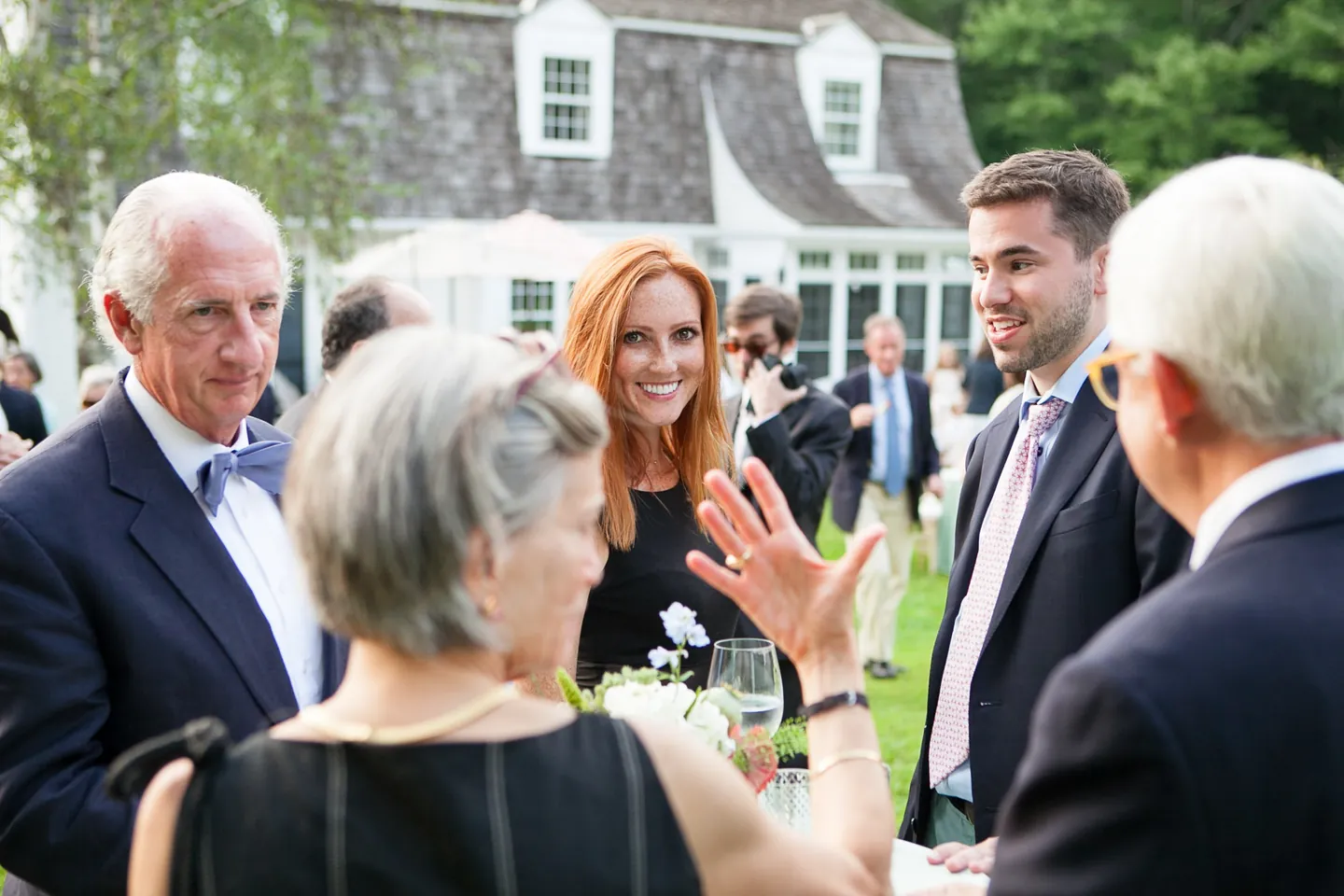 Guests laugh and talk on the lawn during cocktail hour in front of a white house