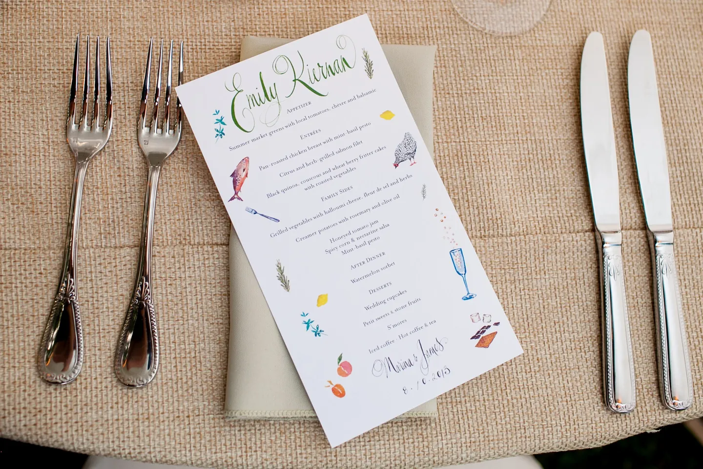 A hand-illustrated menu on burlap between polished silver forks and knives