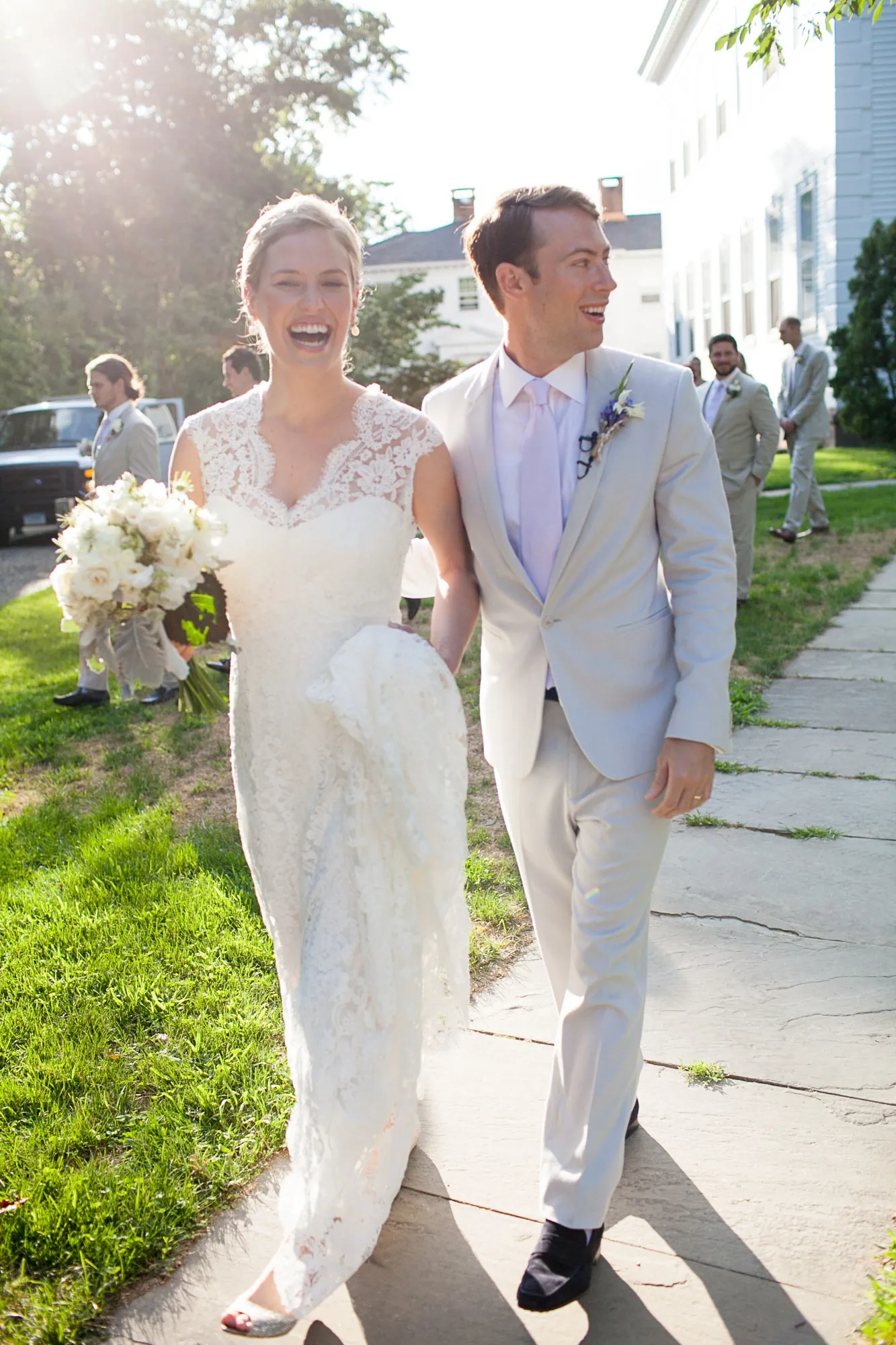 Marina and James walk arm in arm along a leafy sidewalk, laughing