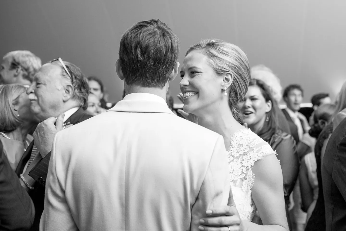 Black and white frame of the bride beaming over the groom's shoulder as they dance