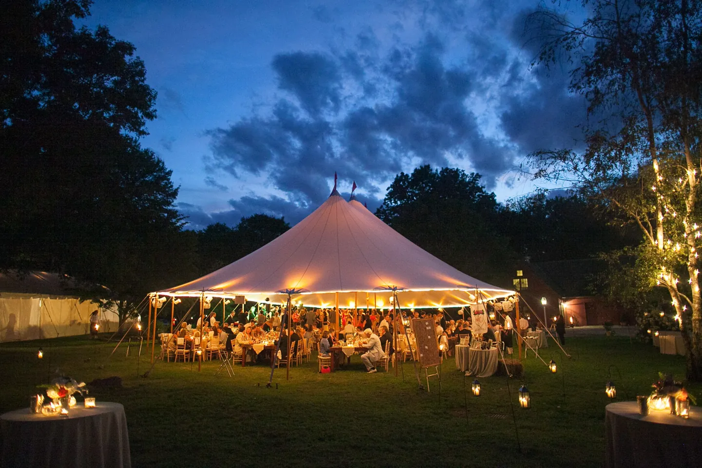 The sailcloth tent glows among dark trees under a deep blue dusk sky