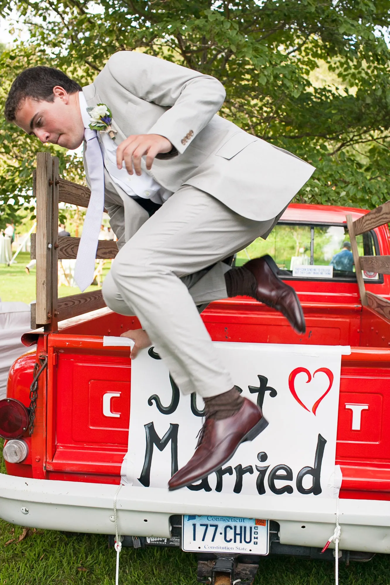 The groom leaps off the tailgate of the red pickup above the Just Married sign
