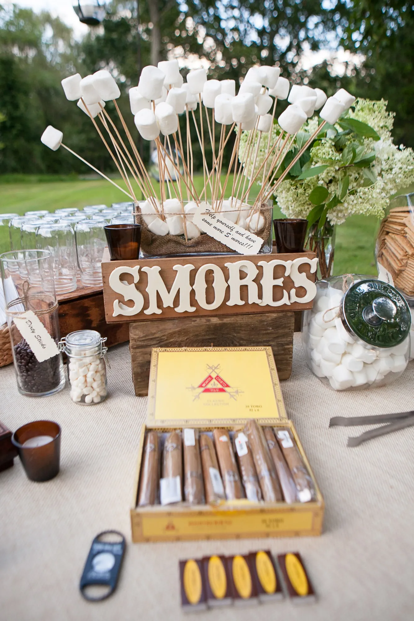 A s'mores station with a wooden sign, chocolate bars and white flowers