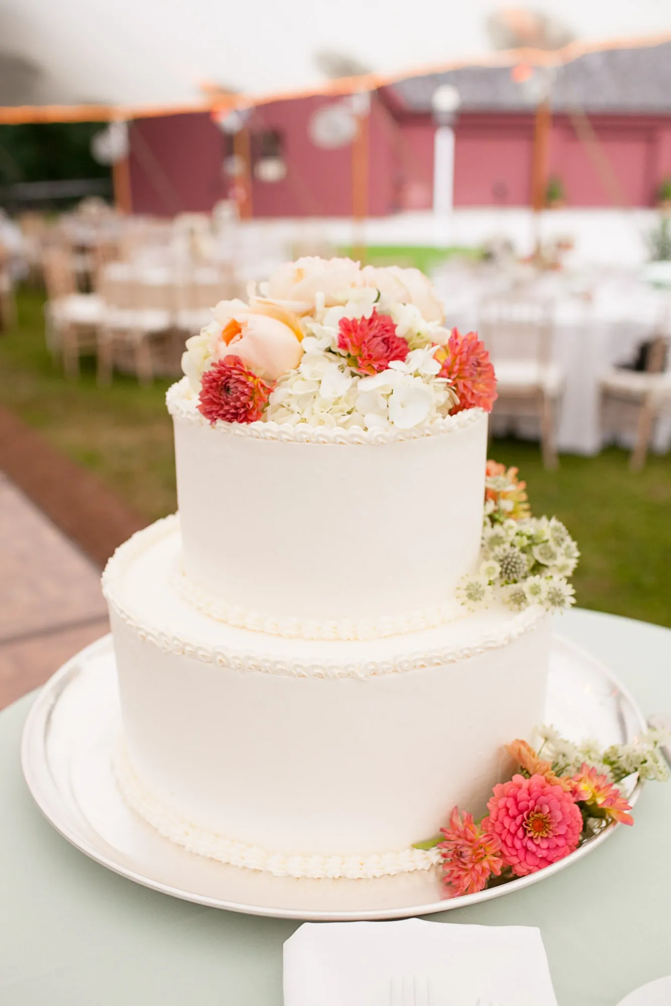 A white tiered cake topped with coral and pink flowers on a reception table