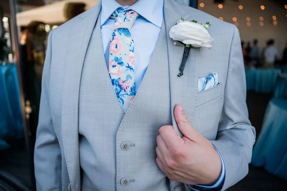 Groom's light grey vest, floral blue and pink tie, and white rose boutonniere up close
