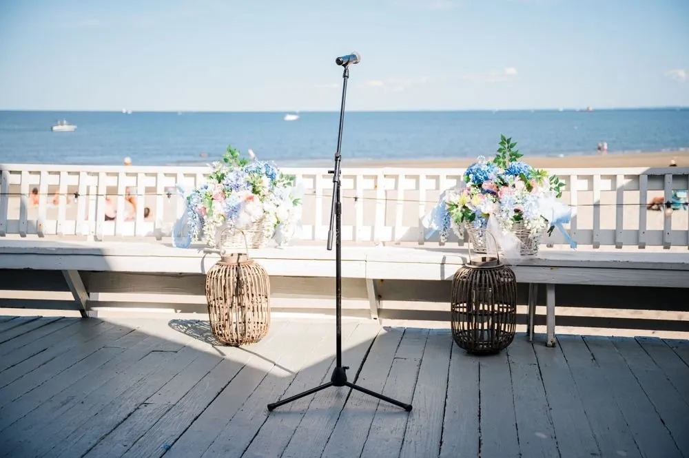 Ceremony setup on the pavilion deck with a microphone stand, lanterns, and hydrangeas facing the water
