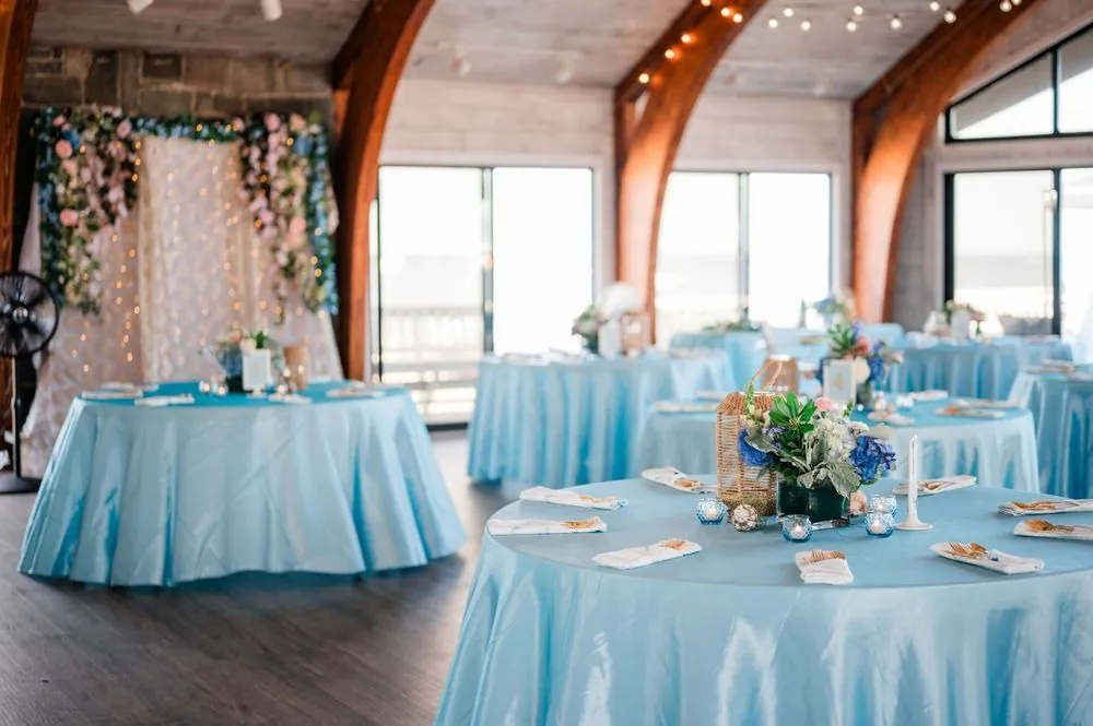 Pavilion reception room with sky blue linens, floral centerpieces, and warm wood beams