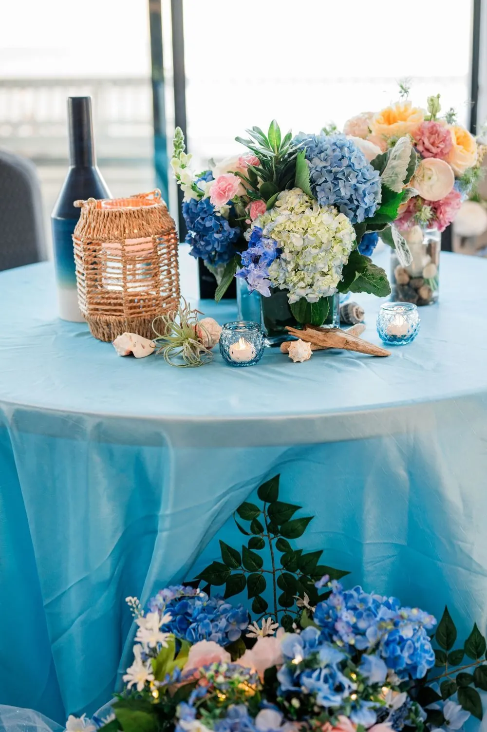 Centerpiece of blue hydrangeas and pink blooms on a sky blue table by the windows