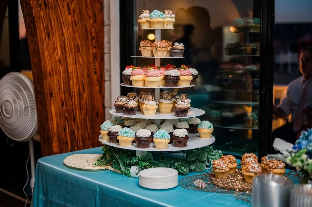 Tiered tower of frosted cupcakes on a blue table beside the pavilion windows