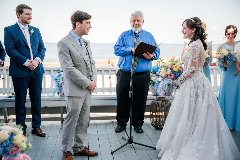 Officiant in a bright blue shirt reads as Mary and Dan face each other on the deck