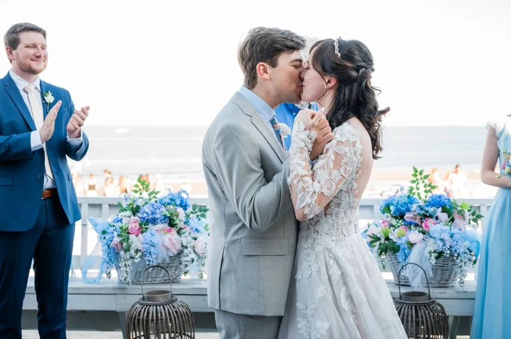 Mary and Dan kiss at the railing as a groomsman in navy claps beside them