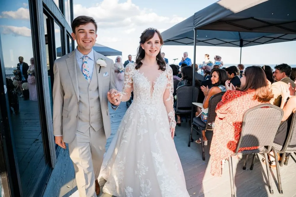 Mary and Dan walk back up the deck aisle grinning as seated guests applaud