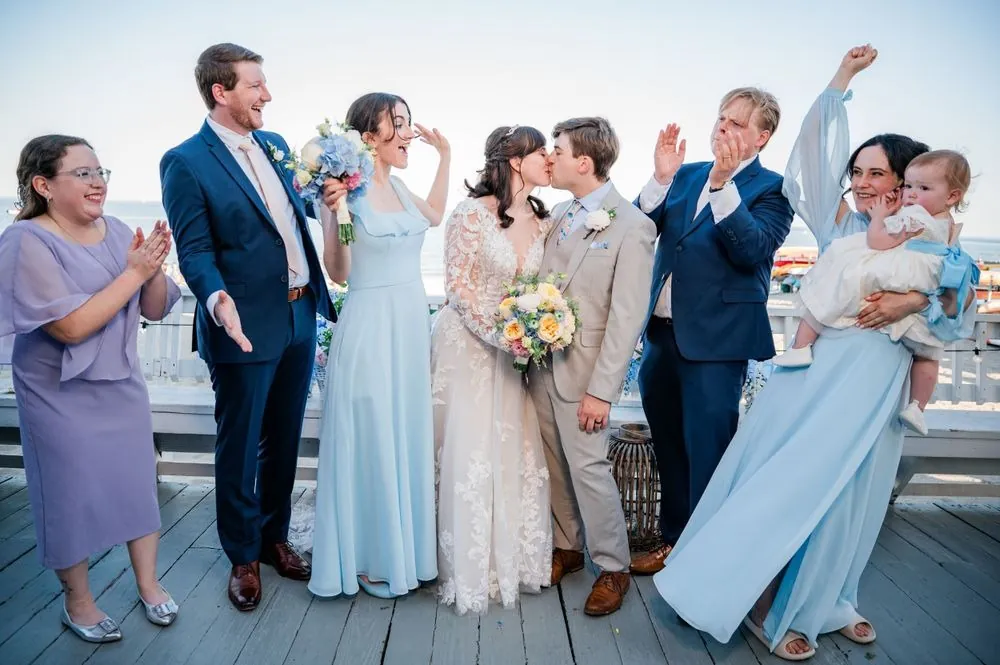 Family and wedding party cheer together on the deck, one man holding a baby