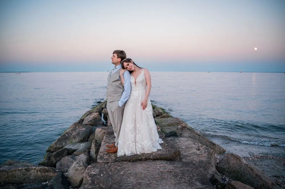 Mary rests her head on Dan's shoulder at the end of a rock jetty with the moon rising