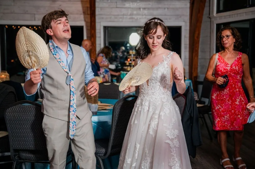 Groom waves a hand fan while the bride laughs beside him during the reception