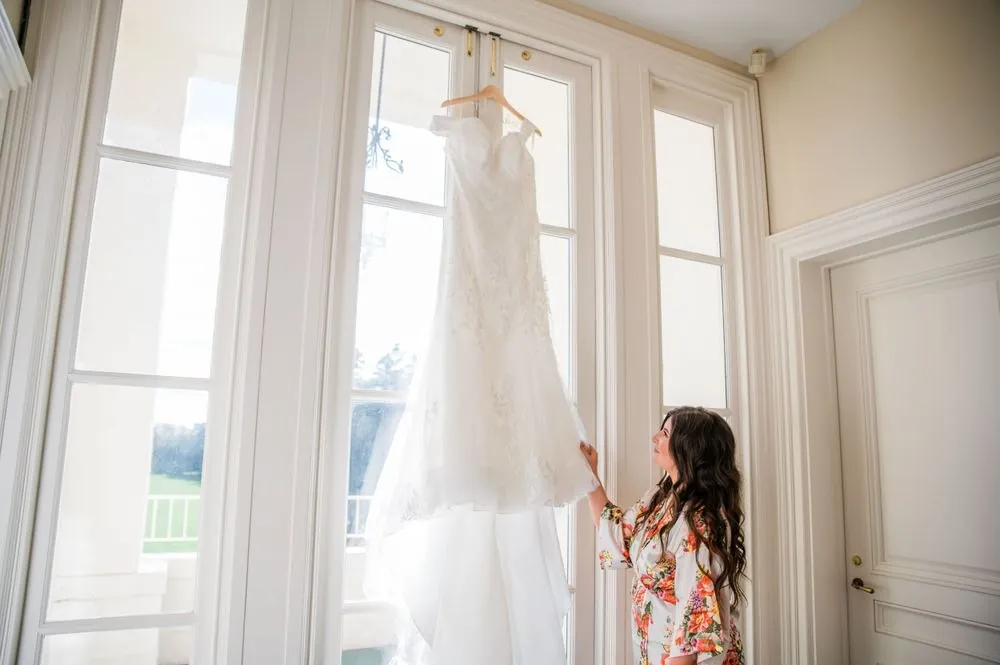 The bride reaches for her gown hanging in a tall window of the mansion