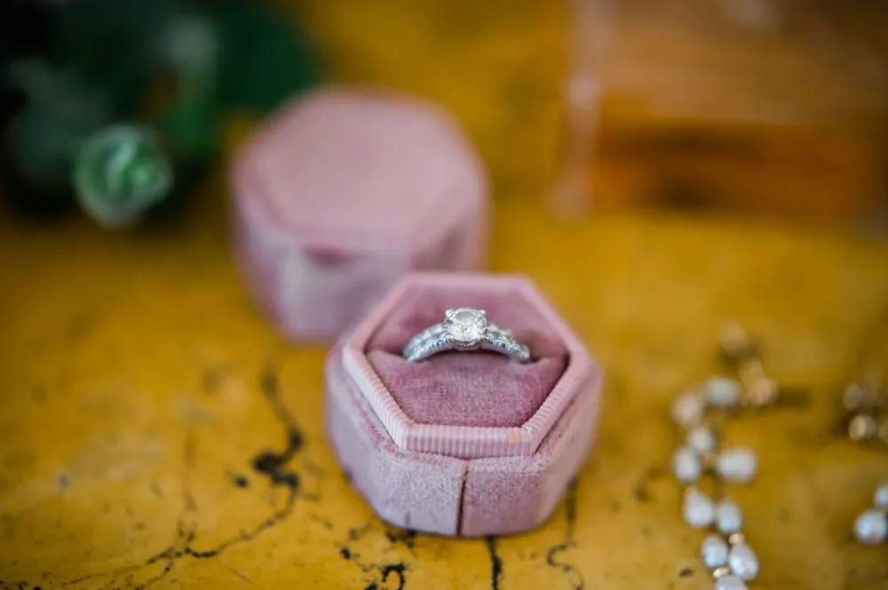 An engagement ring resting in a pink velvet box on a gold textured surface