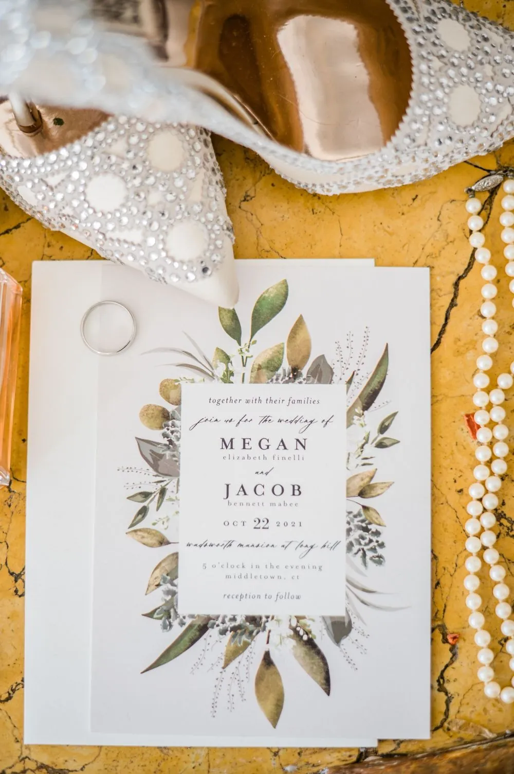 A white invitation suite with a leafy green border set on gold fabric