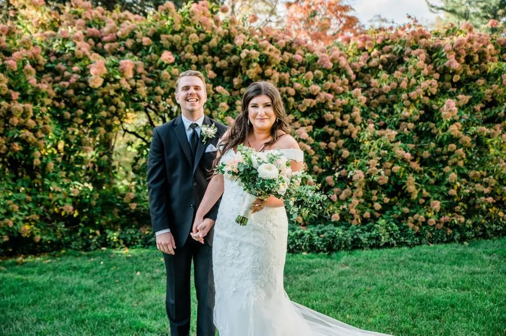 Megan and Jacob laugh arm in arm in front of pink and rust hydrangeas