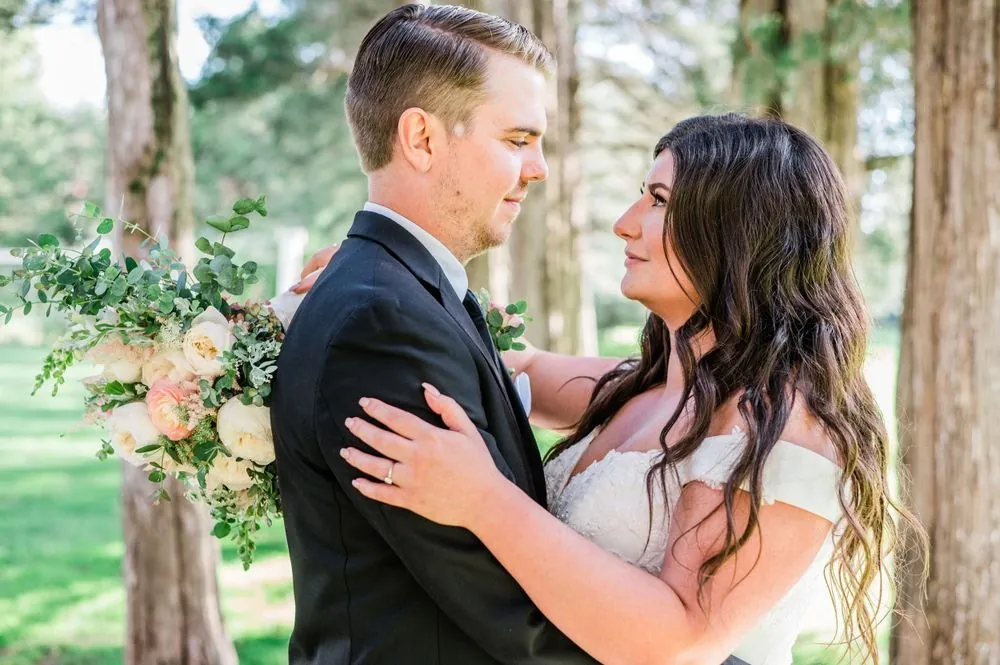 The couple holds each other close under the trees with soft light behind them