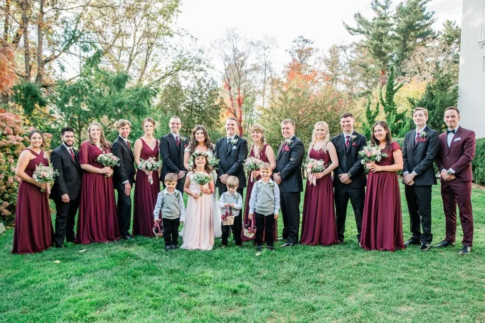 The full wedding party in burgundy and black lined up on the lawn with children in front