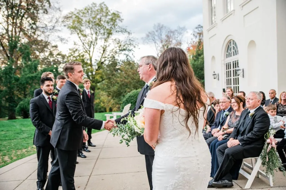 The groom steps forward to meet the bride partway down the courtyard aisle