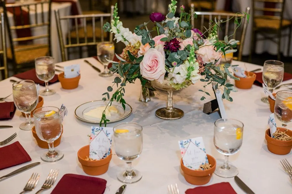 A reception table with burgundy napkins, gold chairs and a tall floral centerpiece