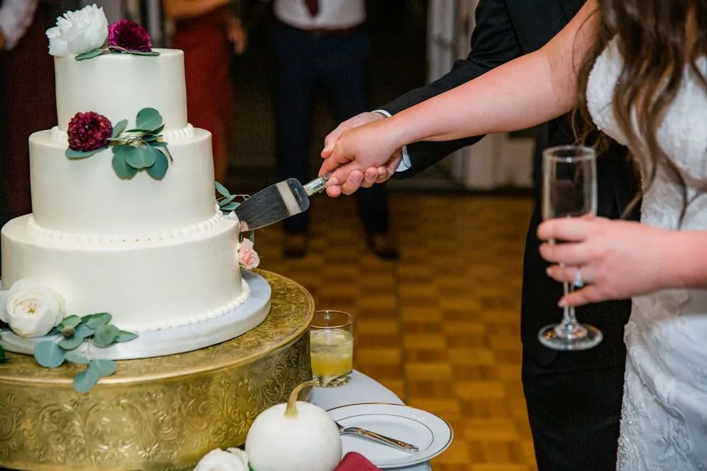 The couple cuts a white tiered cake topped with deep red roses