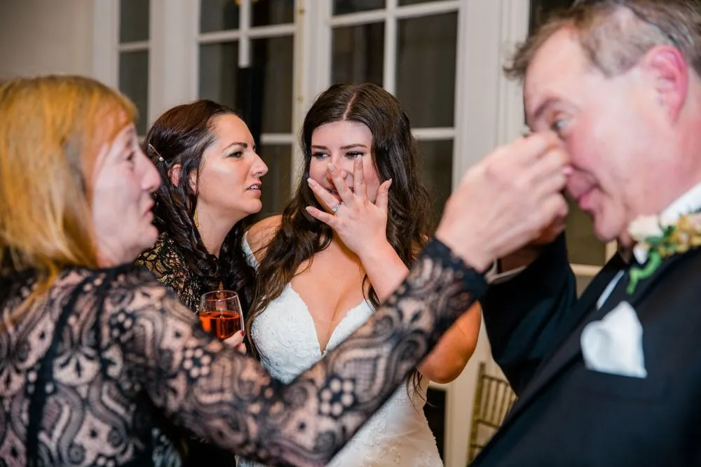 The bride covers her mouth in happy tears as family members wipe their eyes