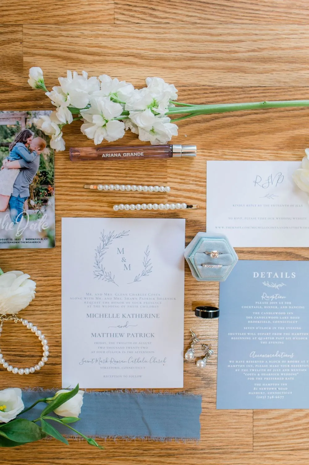 Pale blue invitation suite, pearl hairpins, and white blooms laid out on a wood table
