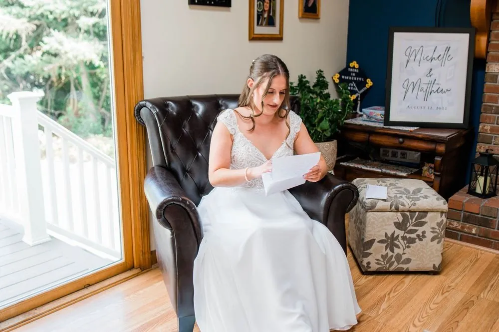 Bride reads a letter in a leather armchair beside a sign with her and Matt's names