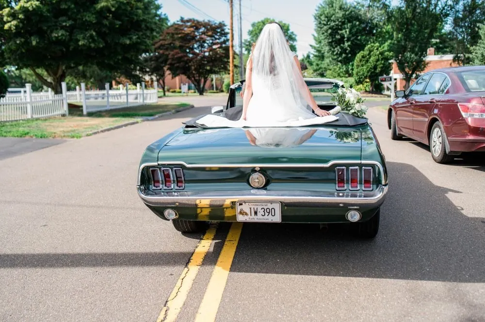 The green convertible drives off down a quiet street with the bride's veil trailing
