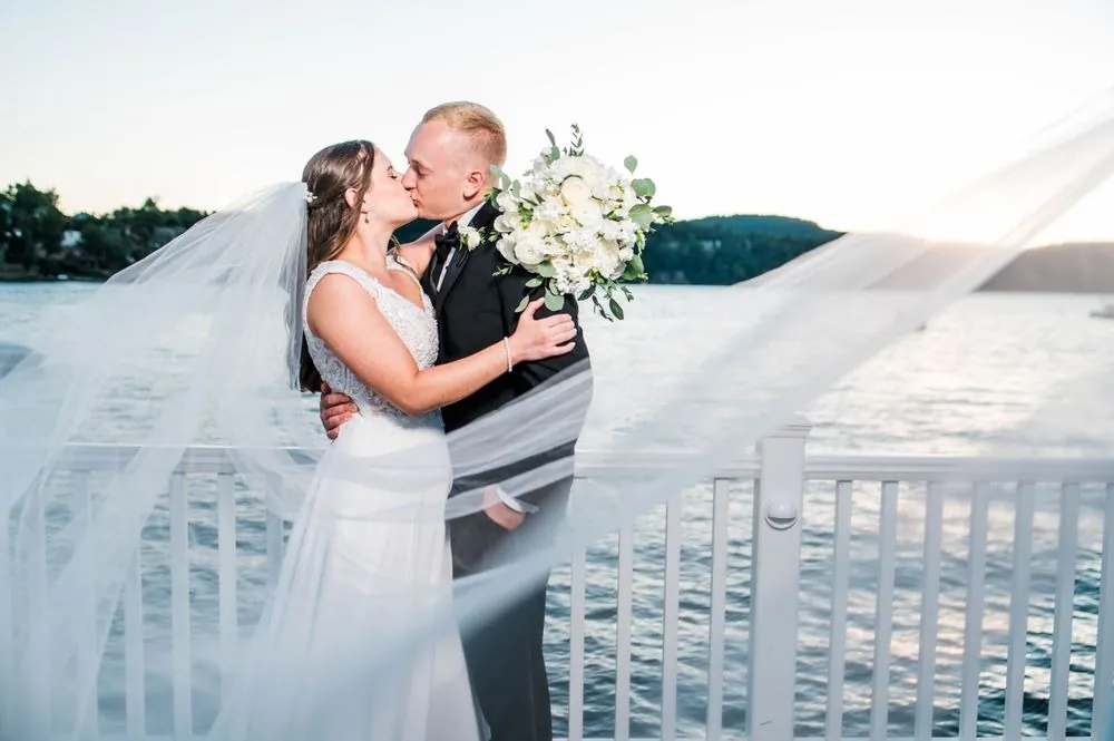 Michelle and Matt kiss on the lakeside deck as her long veil blows across the frame