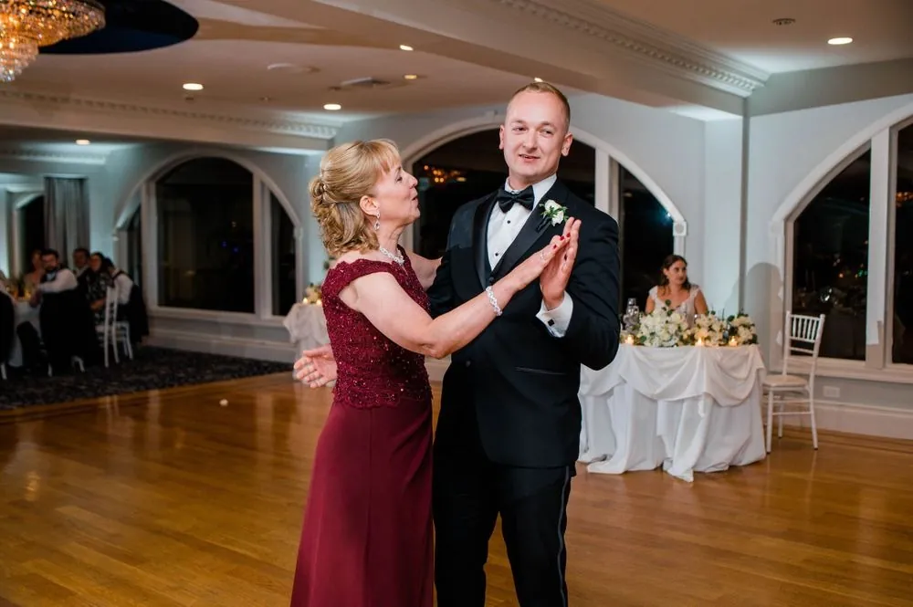 Groom dances with a woman in a burgundy dress on the polished ballroom floor