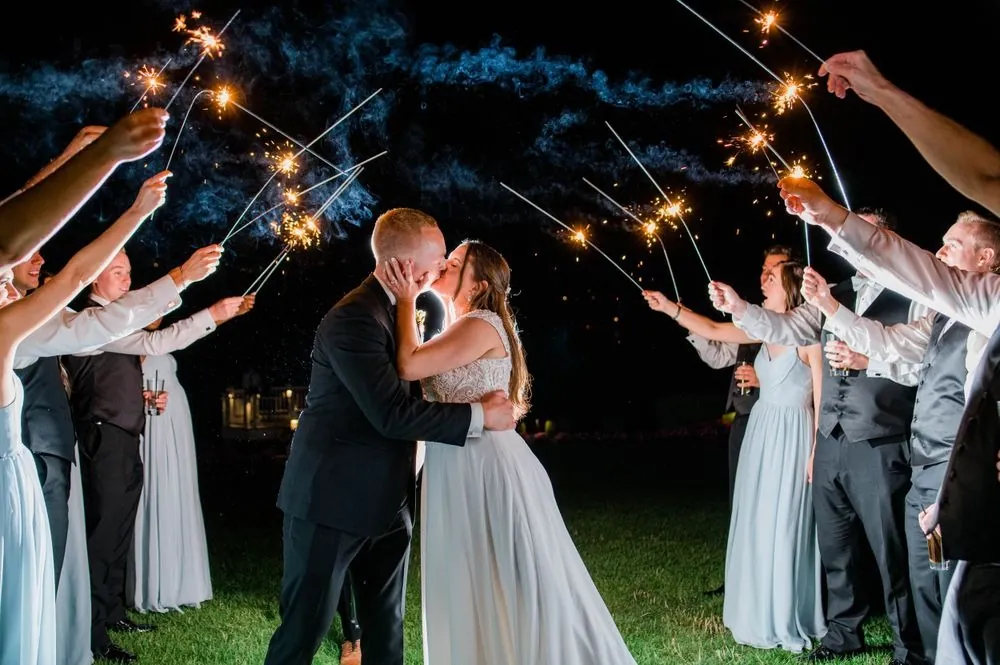 Michelle and Matt kiss beneath a tunnel of sparklers held by guests outside