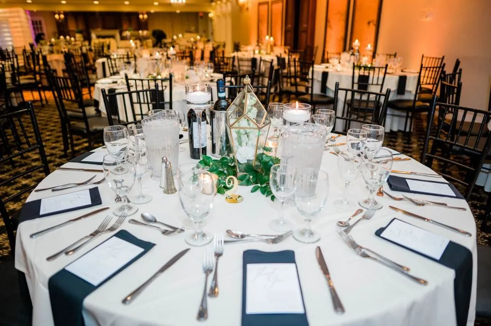 Reception tables set with white linens, black napkins and low centerpieces in warm light