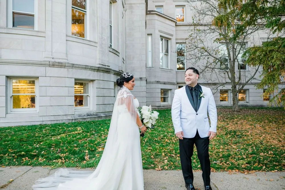 Daniel turns to see Natalie on a leaf-covered sidewalk outside the marble library