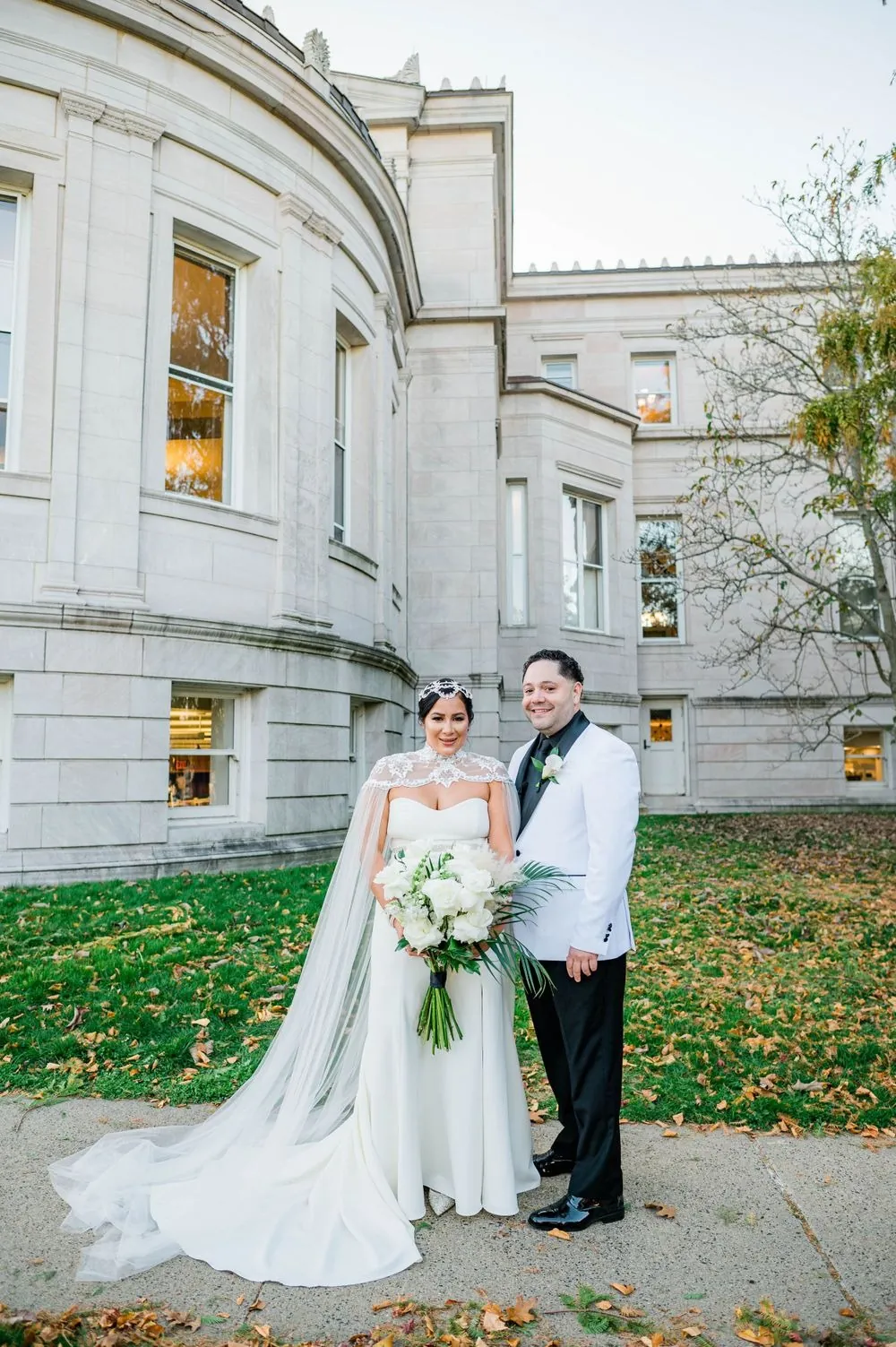 The couple stands together on the lawn beside the stone library