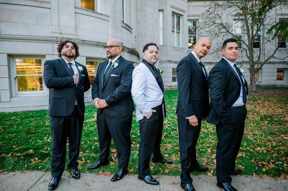 The groom and groomsmen stand on the lawn in front of the marble building