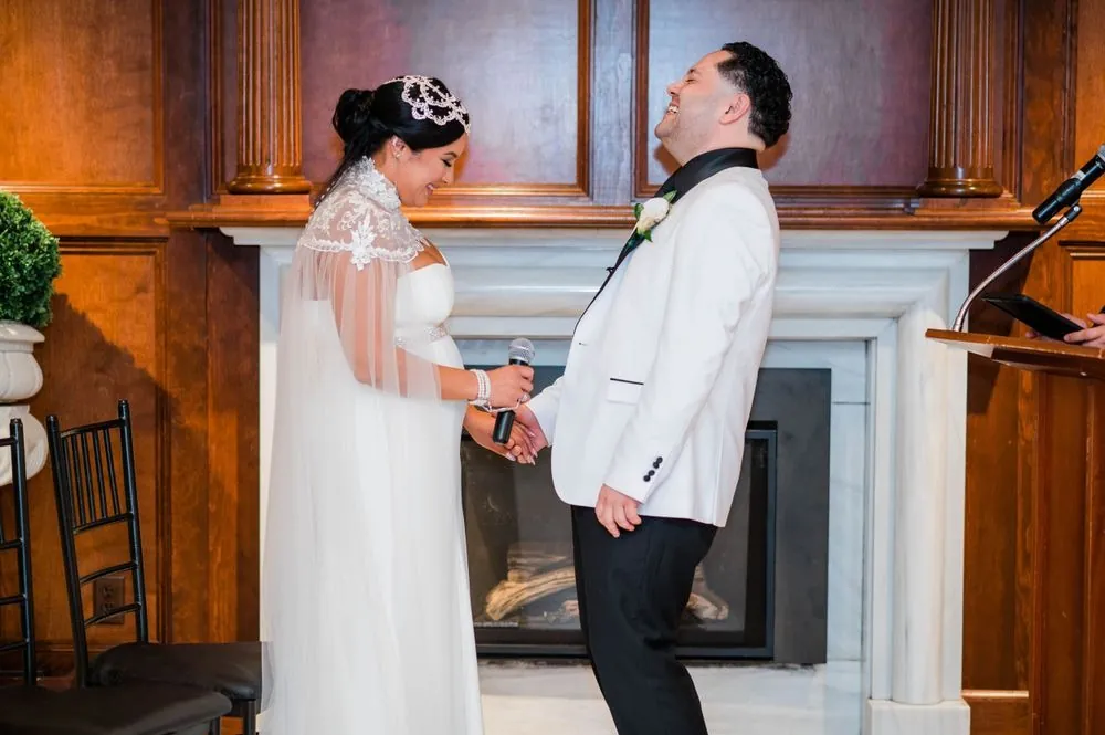 The groom laughs as he holds the bride's hands during the ceremony