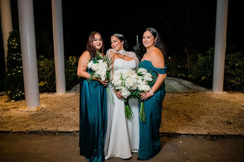 The bride stands with bridesmaids in green gowns under the porch columns at night
