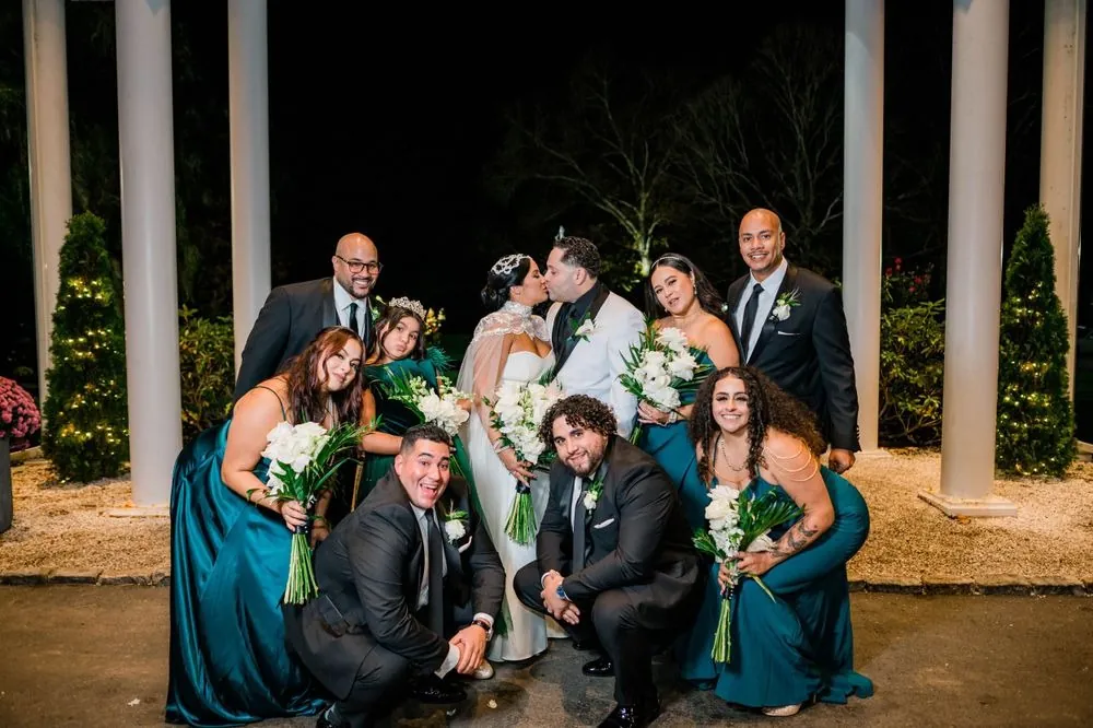 The full wedding party gathers under the lit porch columns after dark