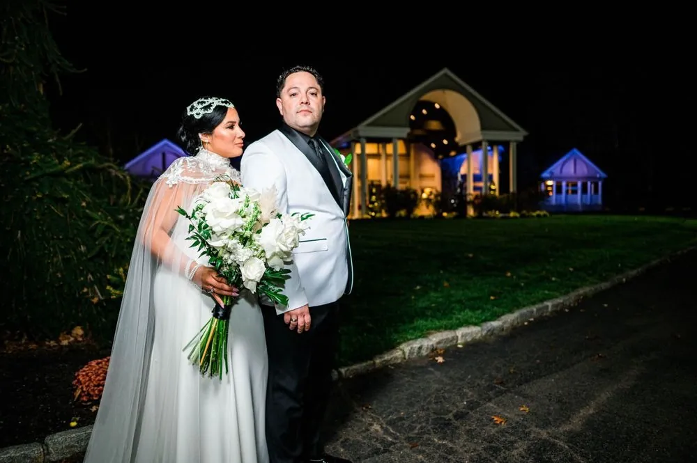 The couple holds each other on the lawn at night with the lit venue behind them