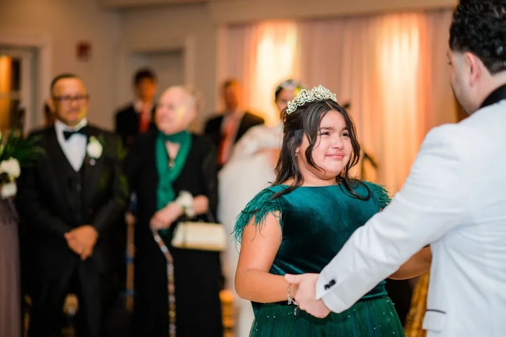A girl in a green velvet dress and tiara tears up while dancing with the groom