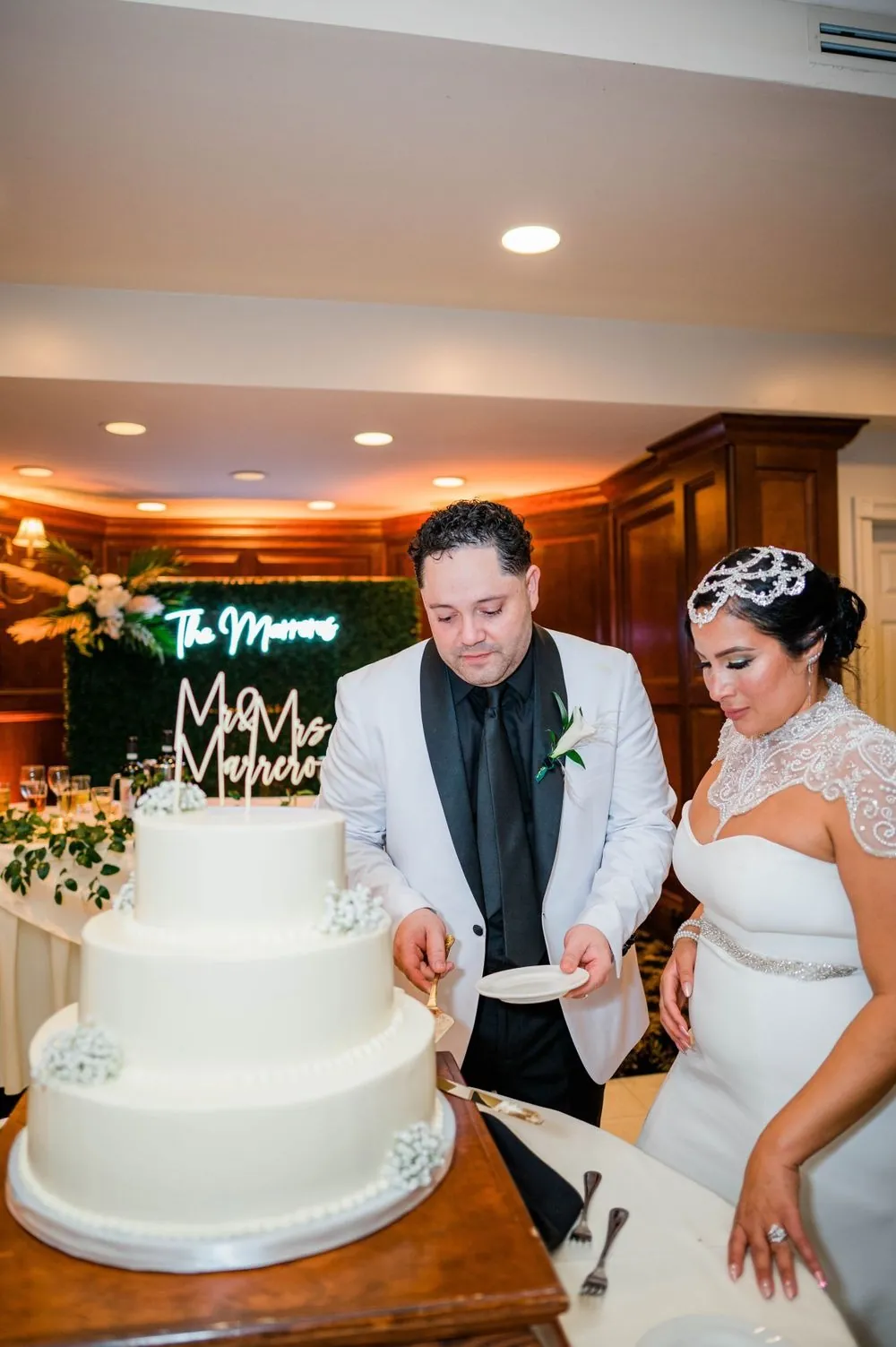 The couple cuts a tall white cake at the edge of the reception room