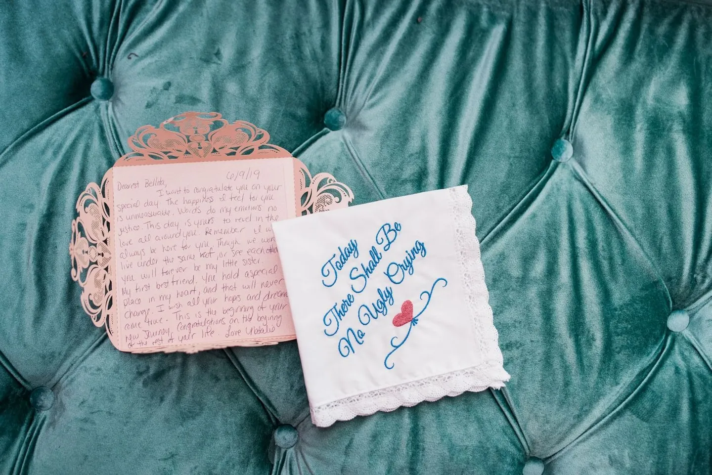 Handwritten letter and an embroidered handkerchief resting on a tufted teal velvet chair