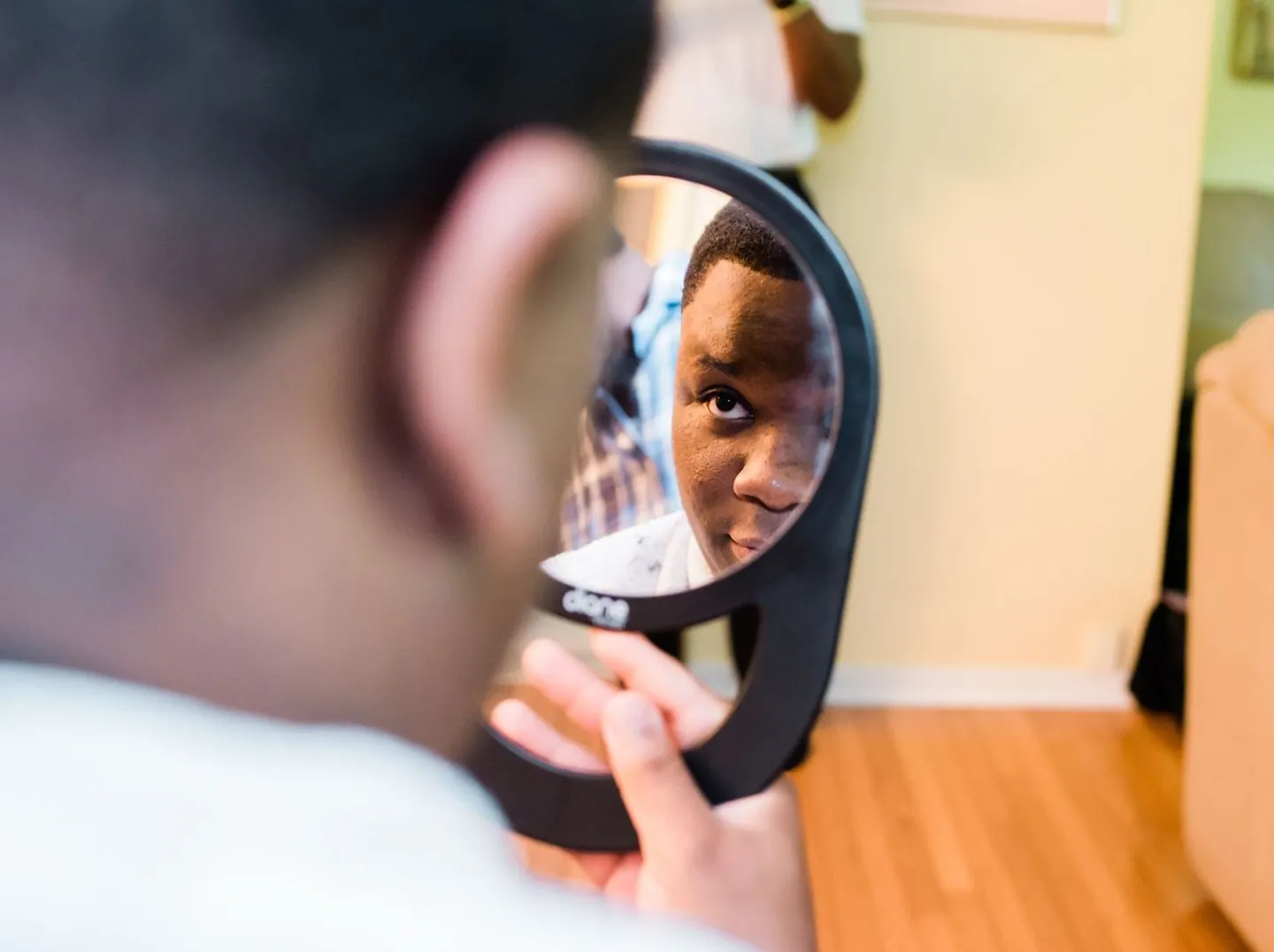 Groom checks his reflection in a round hand mirror while getting dressed