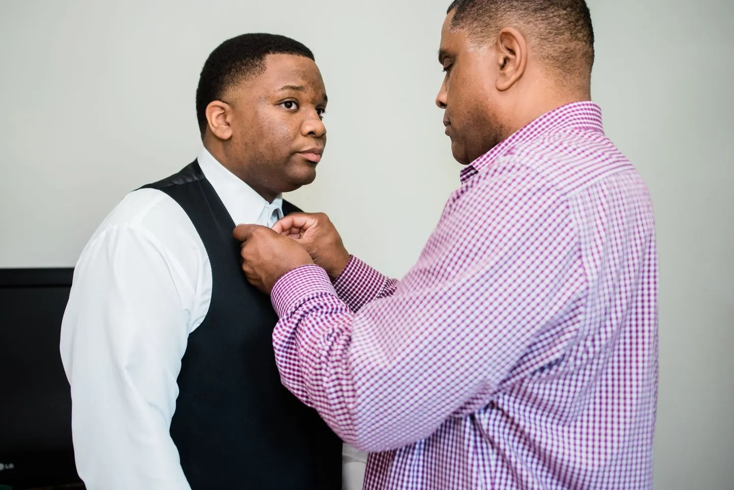 Friend in a checked shirt fastens the groom's bow tie in a bright bedroom