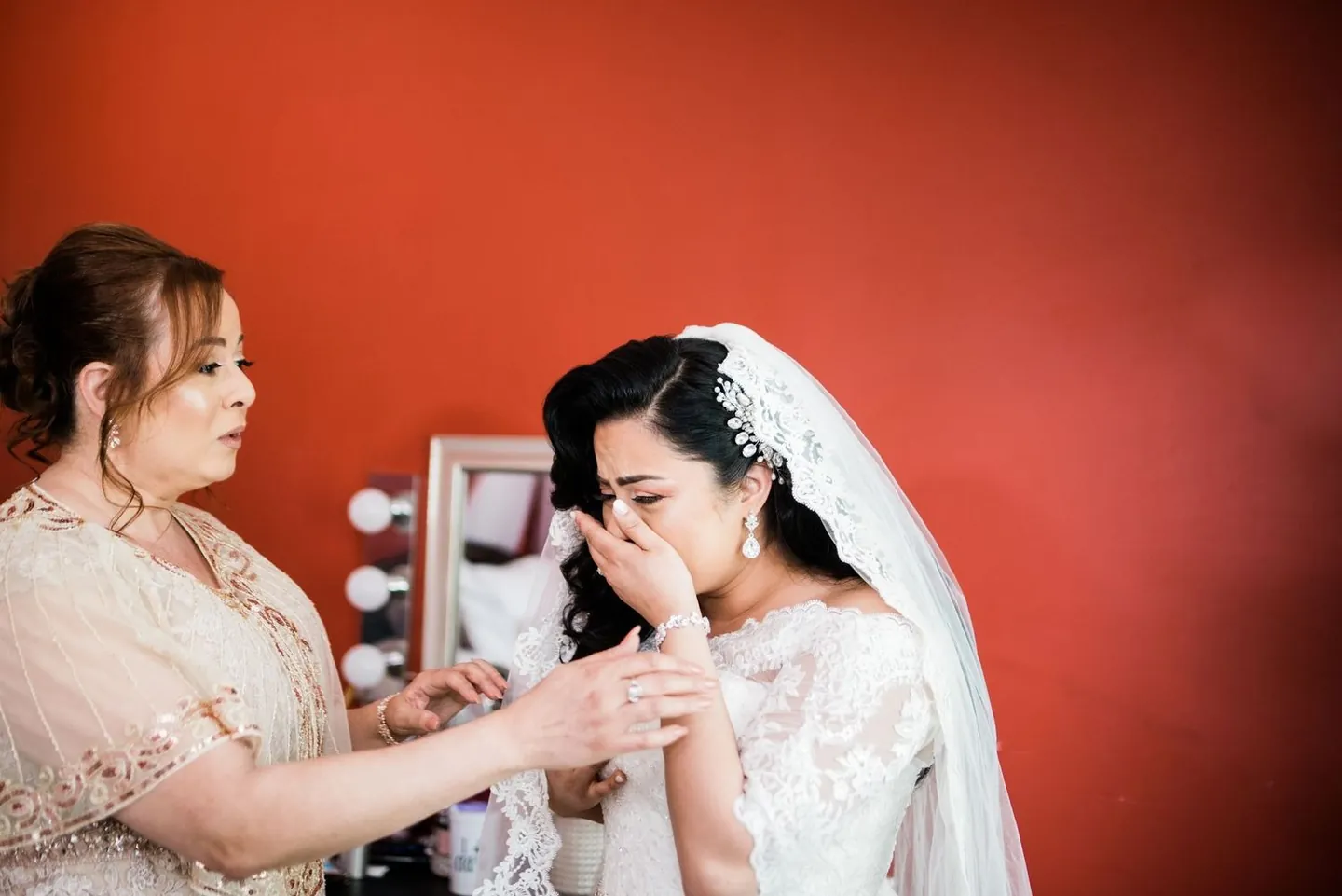 Woman wipes her eyes as she settles the veil over the bride's hair