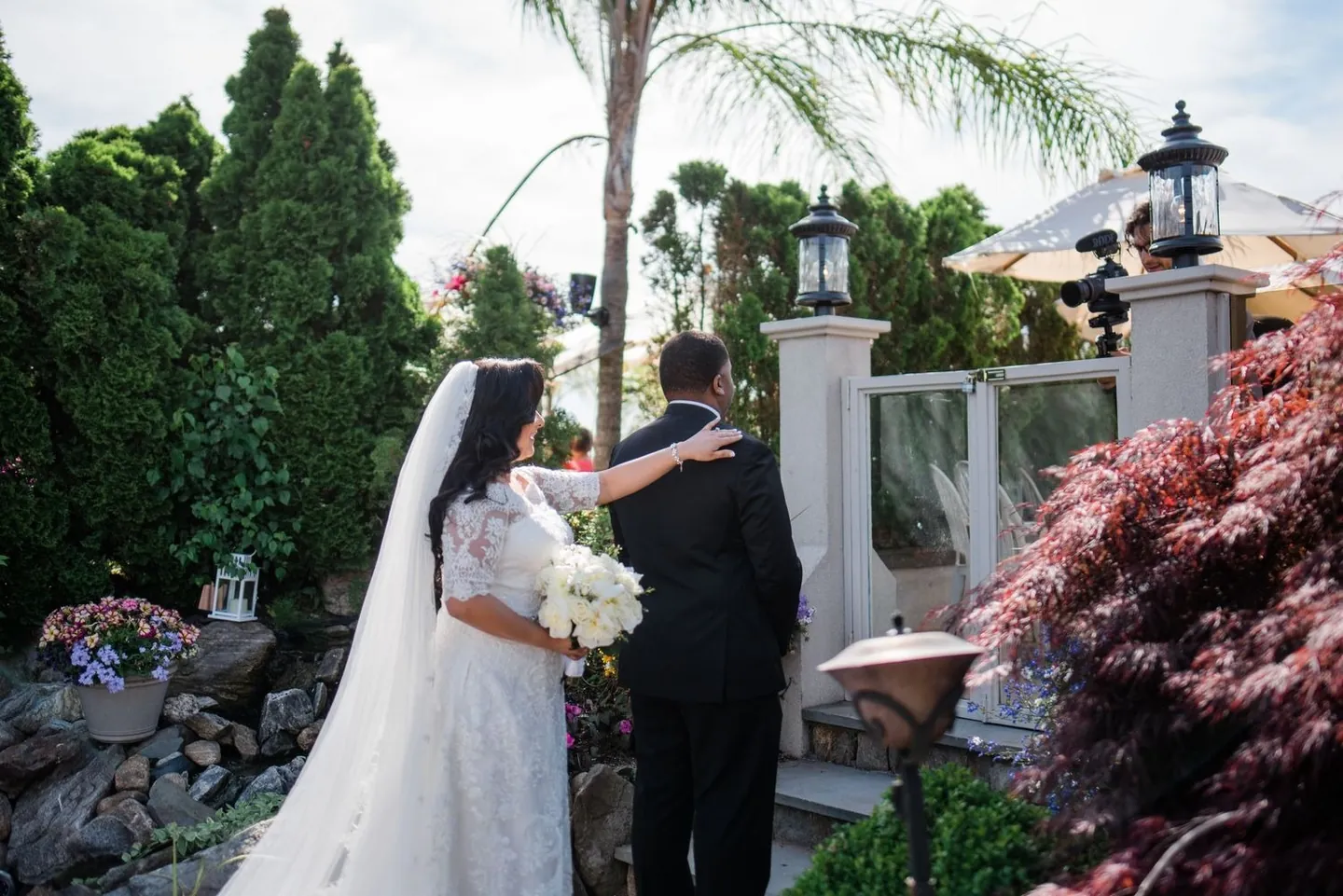 Bride walks up behind the groom in the venue garden for their first look